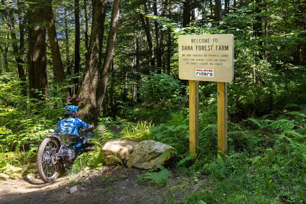 accessible mountain biker riding by dana forest farm sign