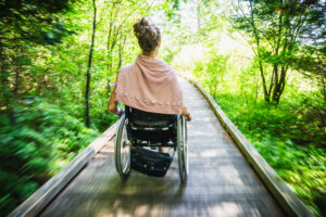 woman with a ponytail moving quickly in a wheelchair on boardwalk through woods