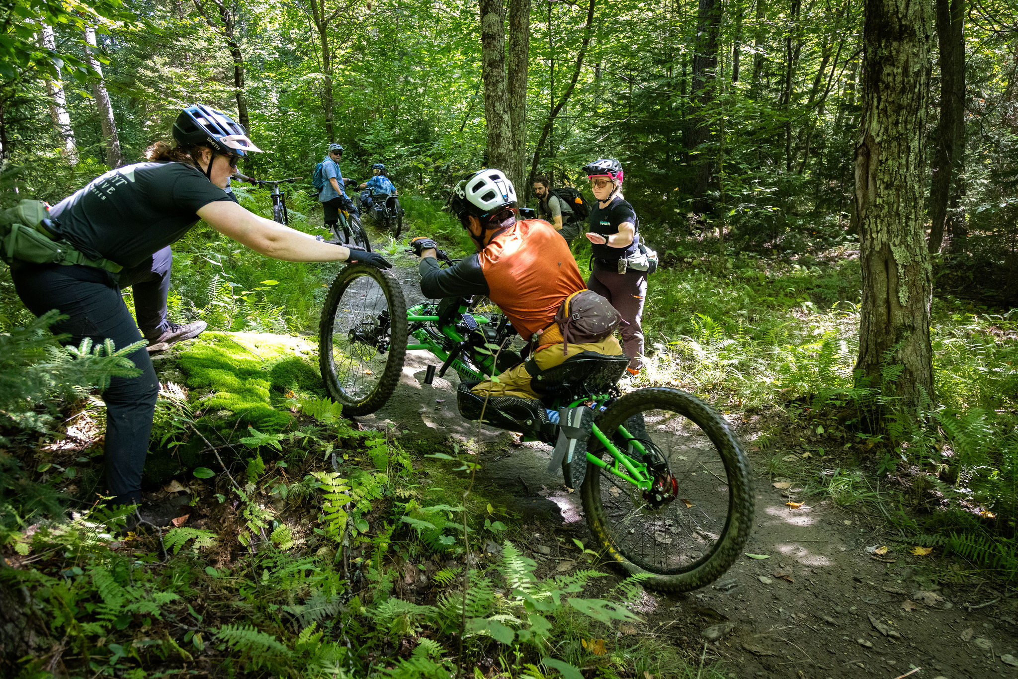 man on adaptive bike going uphill being assisted by a woman