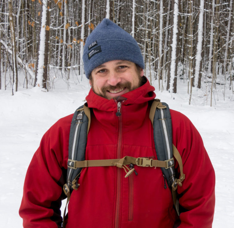 smiling middle-aged man in red jacket and hat standing in snow
